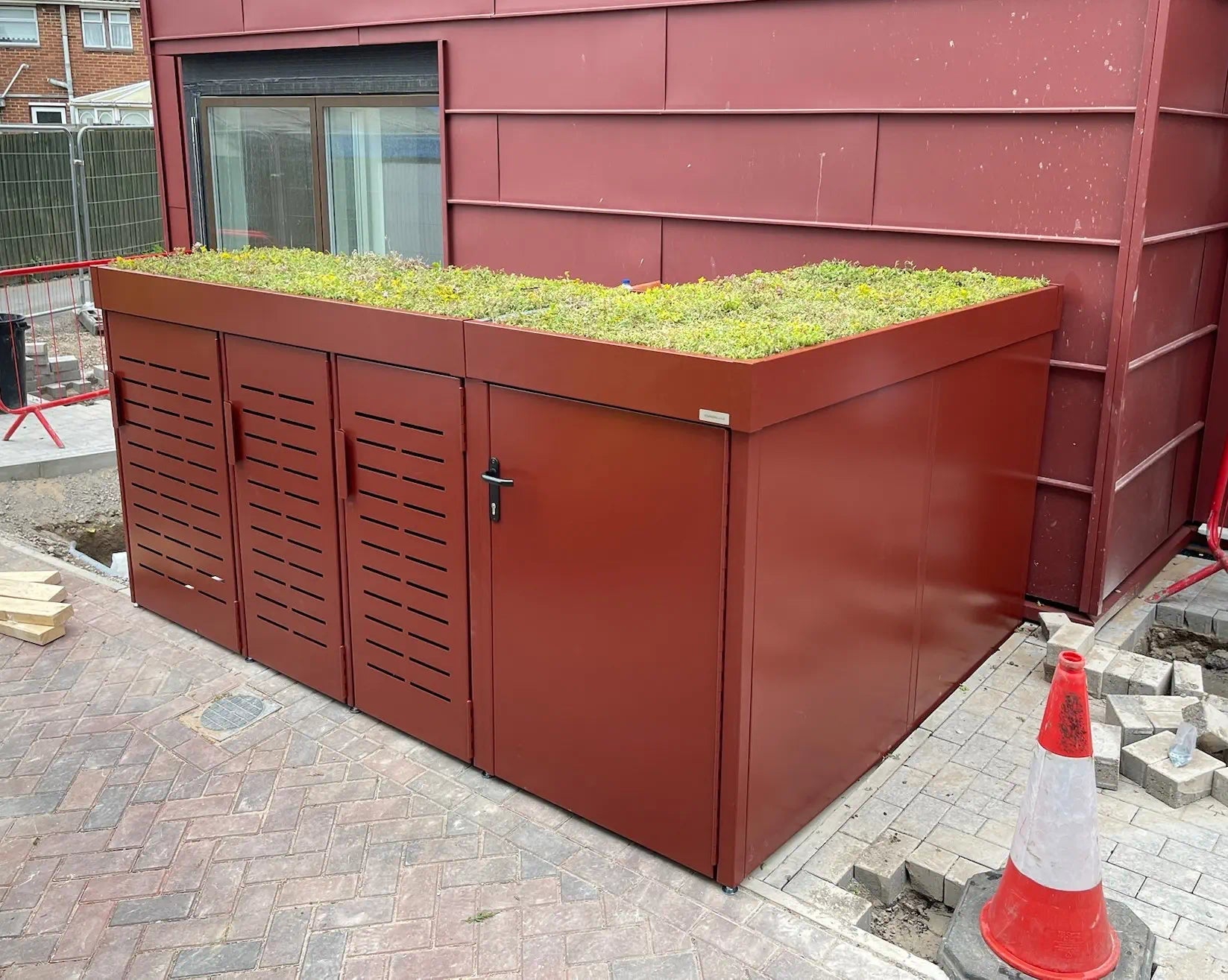 Angled front view of closed metal cycle and refuse store with lush green sedum roof — tailored storage for premium residential developments.