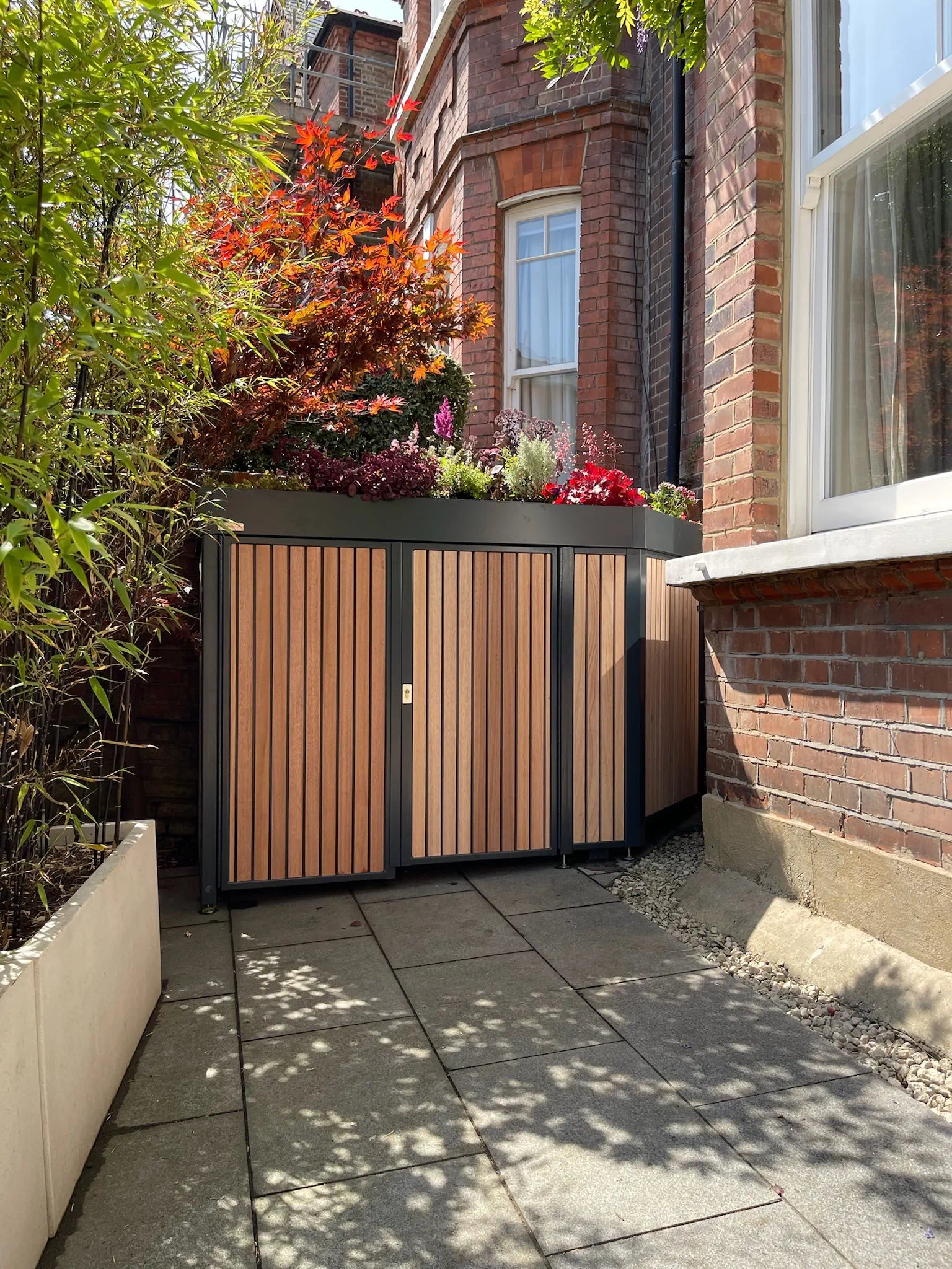 Bike store wrapped around the bay window with biodiverse planted roof, anthracite powder coated metal structure and hardwood timber cladding