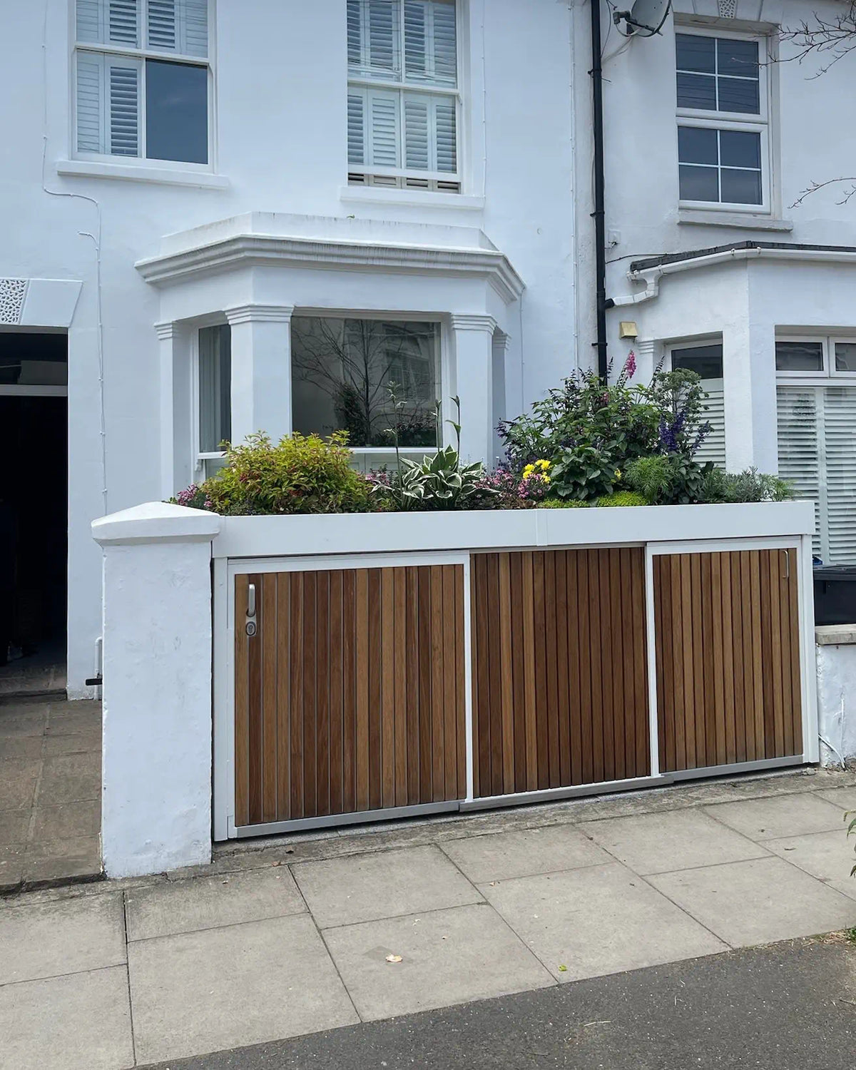 Closed white bin and bike store with sliding doors and a lush planted green roof, viewed from the street.