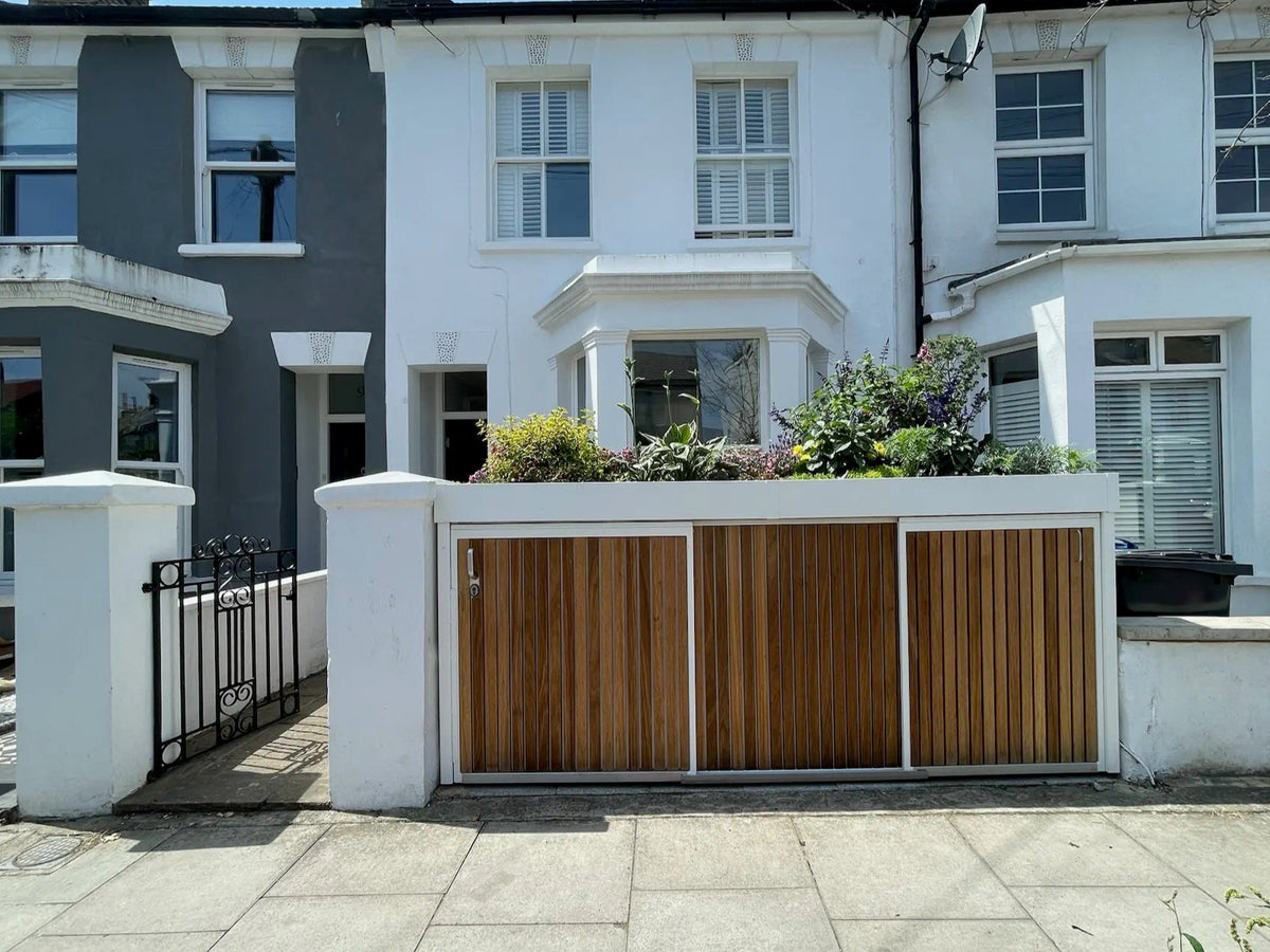 Straight-on view of a white sliding-door bike and bin store with green roof, as seen from the street.