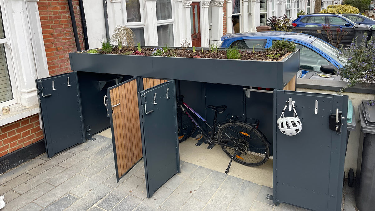 Front view of an open bike storage unit with double hinged doors and a deep planted green roof, showcasing secure storage for multiple bikes