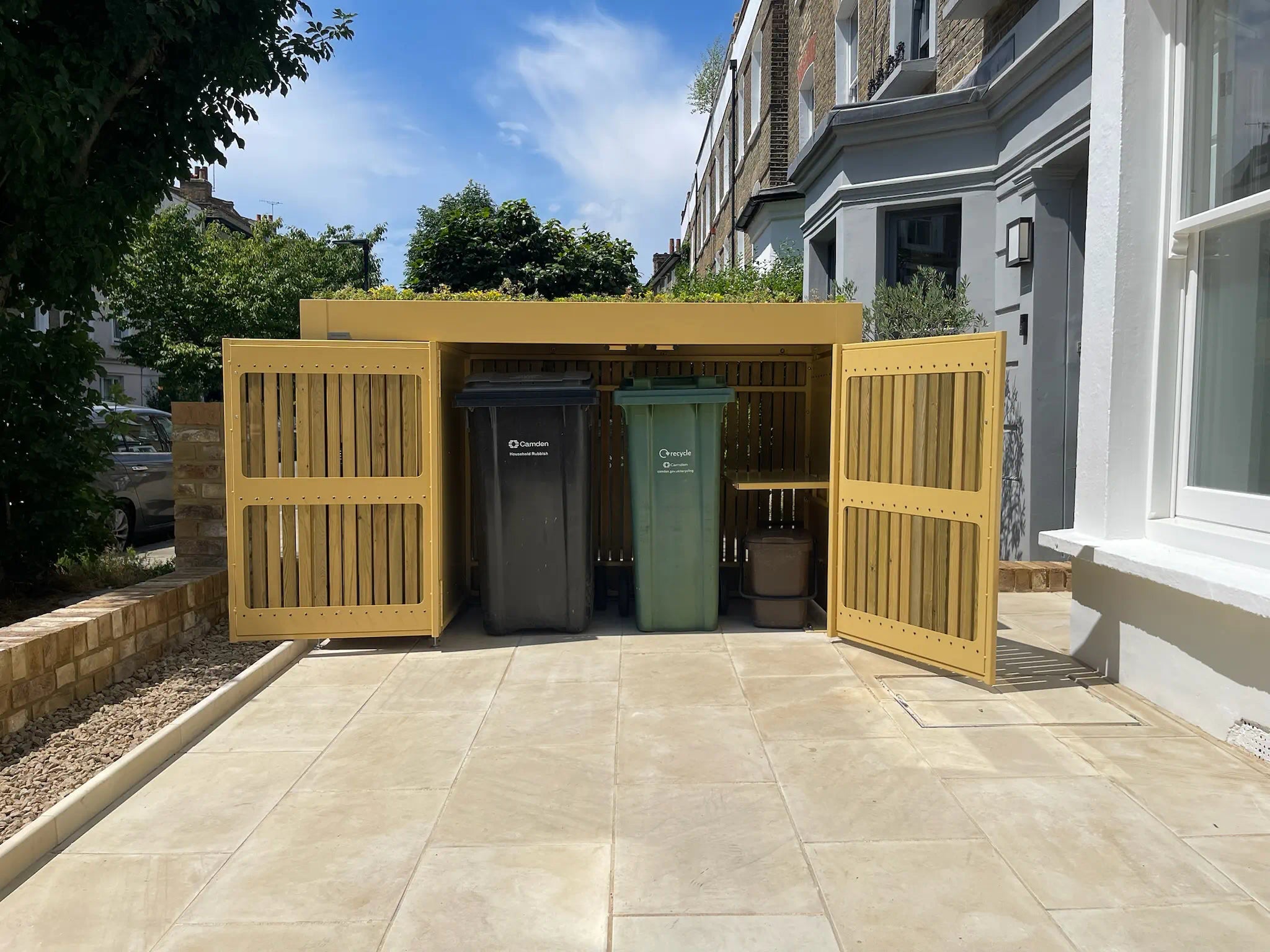 Wheelie bins shown inside open green roof bin store in a London front garden.