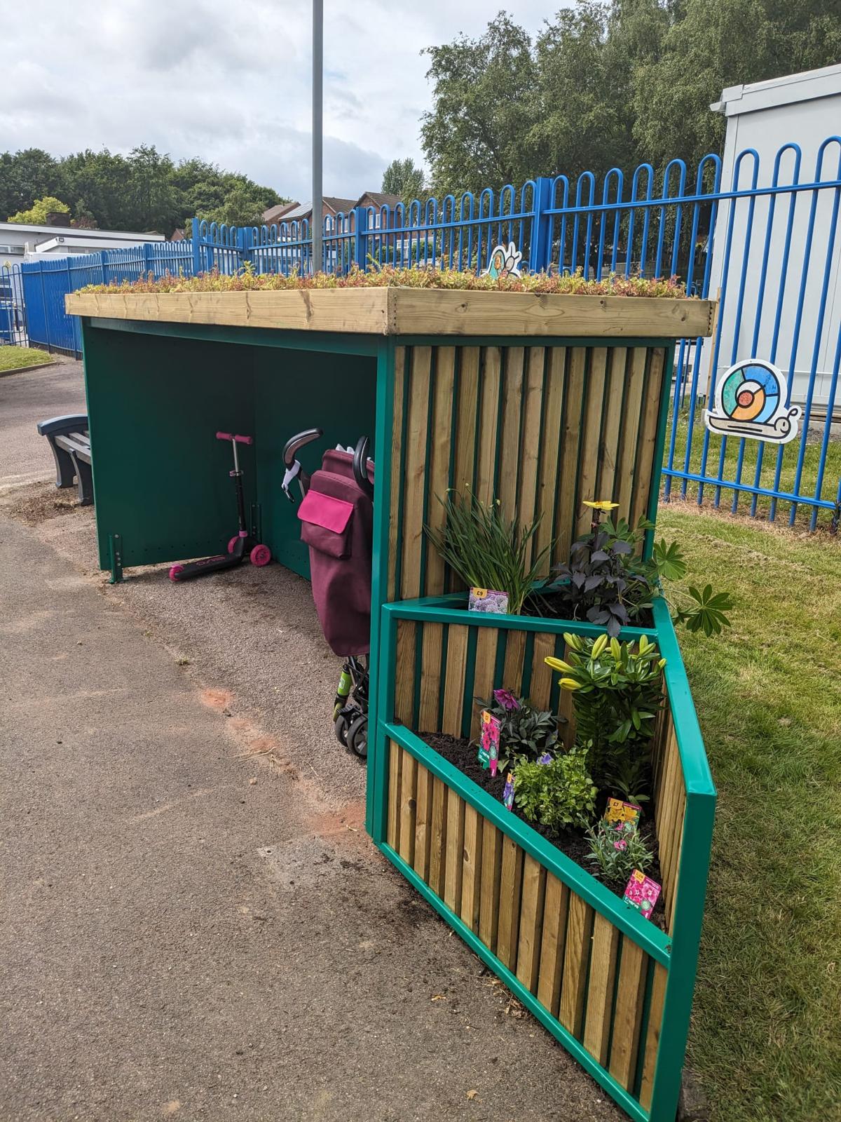 Green roof buggy shelter for schools, offering weather-protected storage for prams and pushchairs with sustainability in mind.