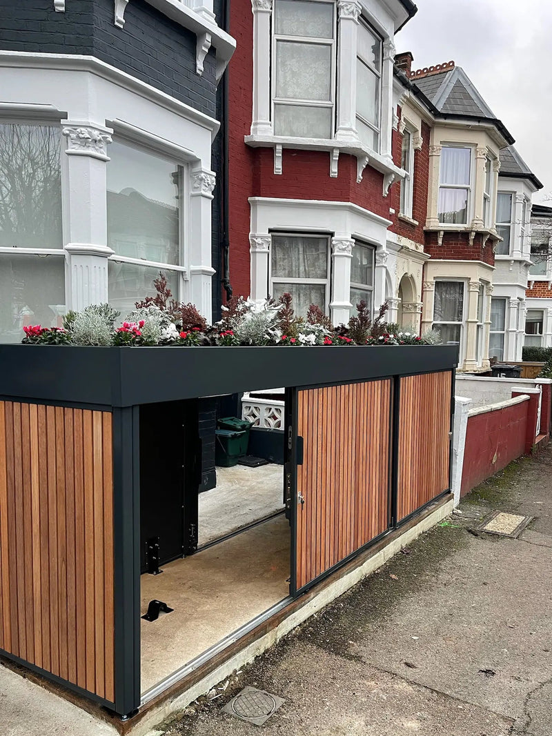 Angled approach view of anthracite grey front garden bike store with sliding doors open in a modern London frontage