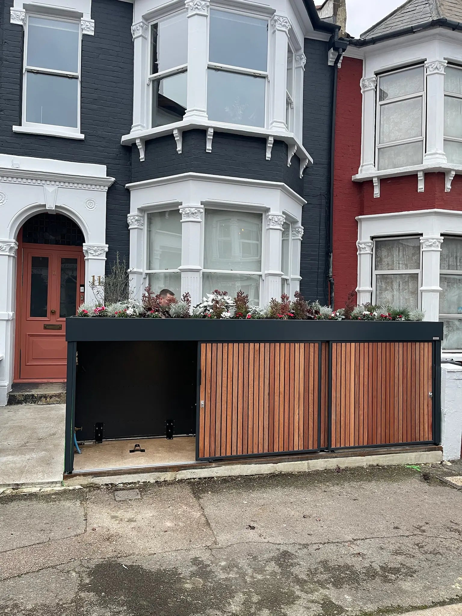 Front view of anthracite grey bike store with sliding doors open, revealing secure bicycle storage in a London front garden