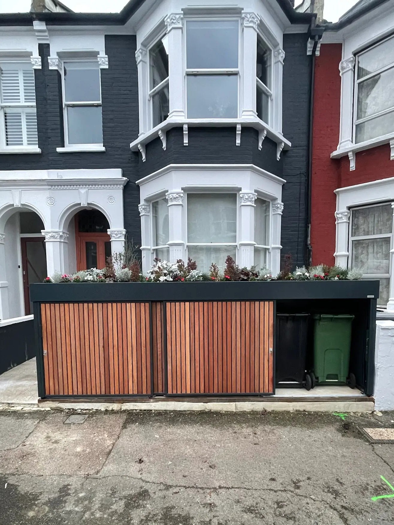 Front view of anthracite grey bin store with large hinged door open, showing concealed wheelie bin storage at street level