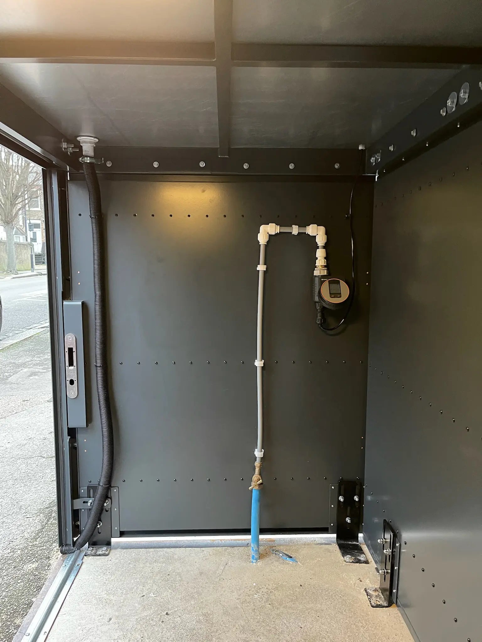 Interior view of full metal bike store with concealed irrigation system beneath planted roof in a London front garden