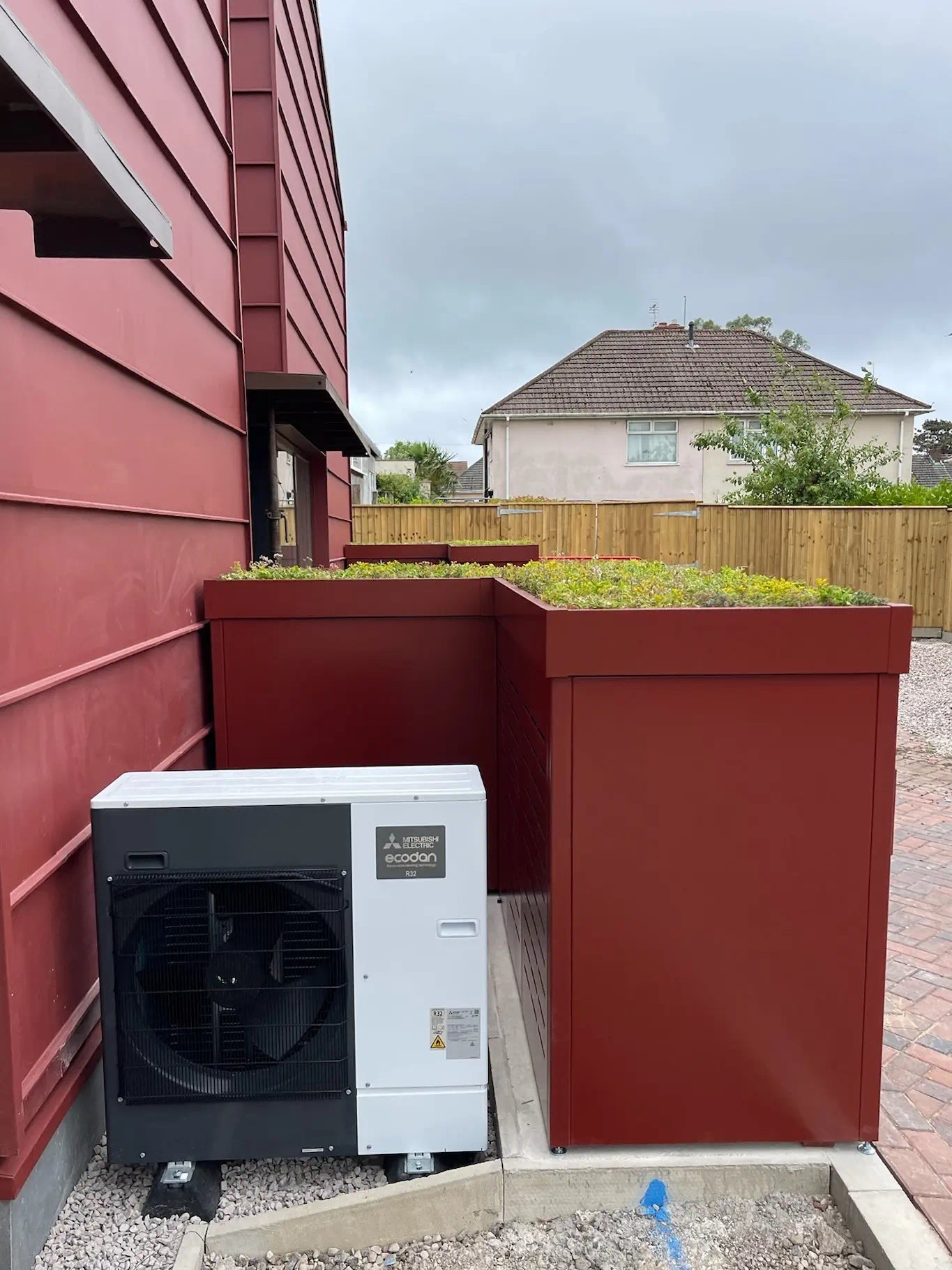 Side view of L-shaped bike and bin store wrapping around outdoor air con units — clever use of space in high-end London residential project.