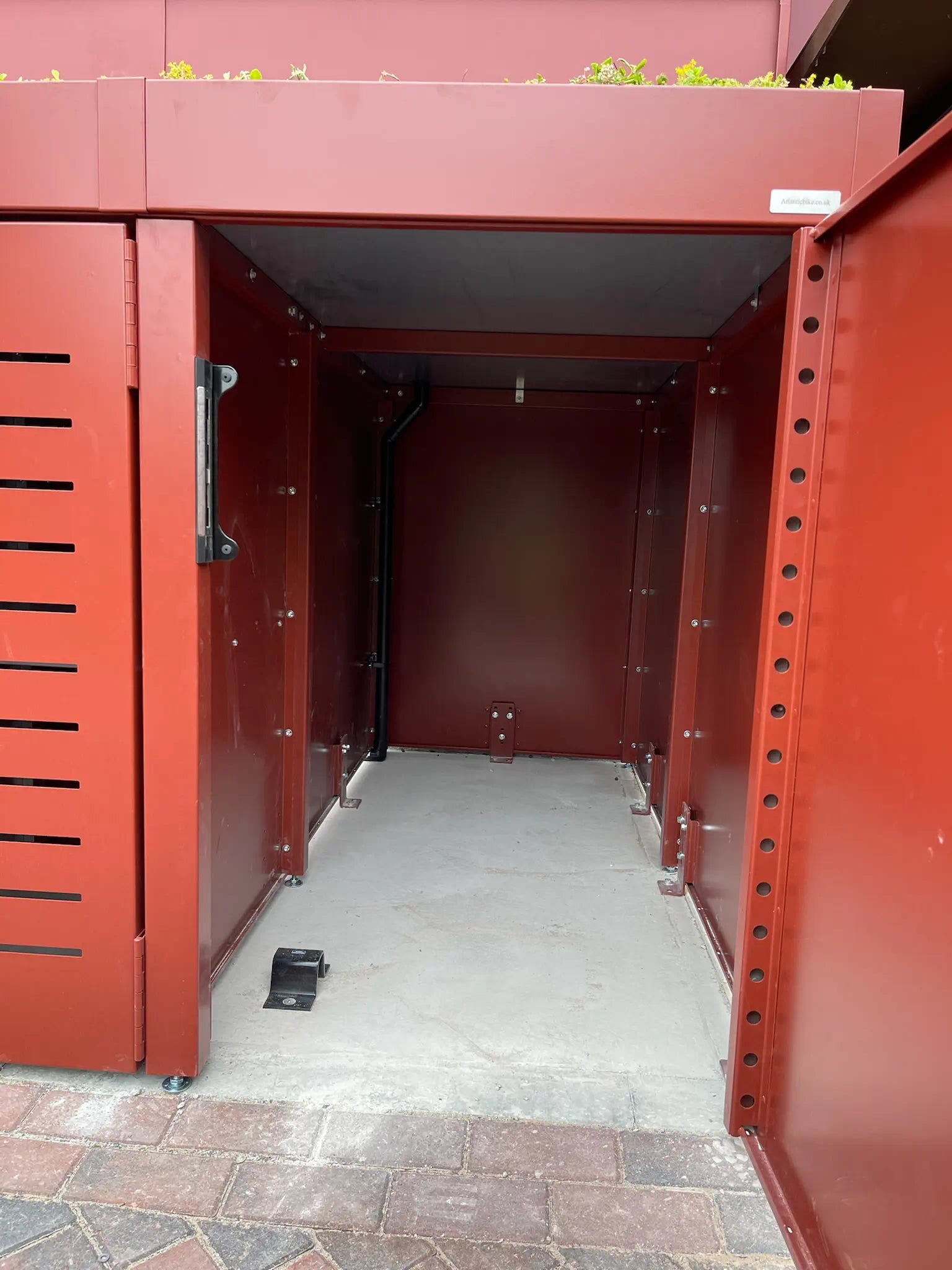 Cycle storage compartment open, revealing secure end-on bike access within red oxide powder-coated metal store — ideal for London residential settings.