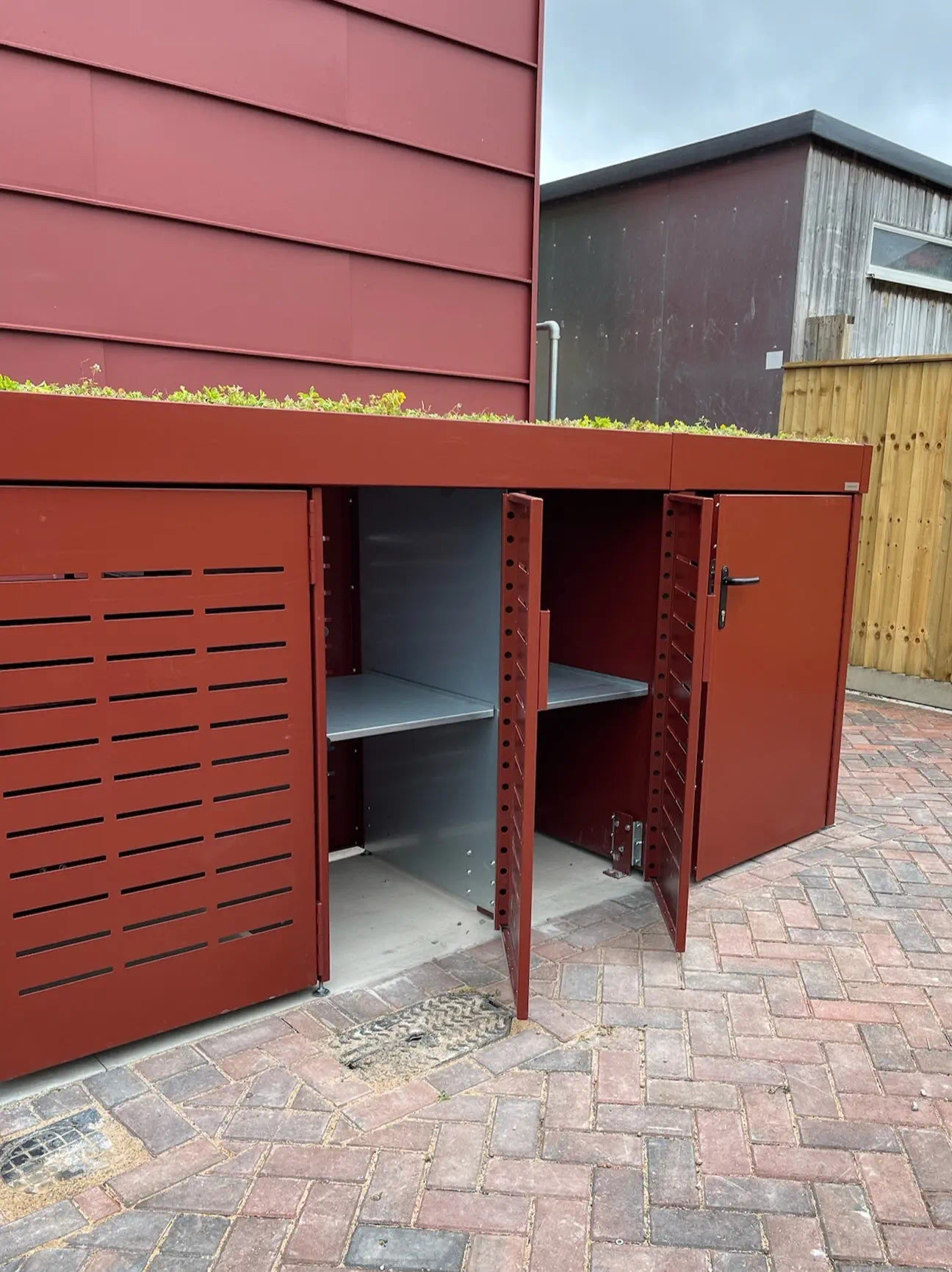 Front view of bin store with partially open refuse door and visible galvanised steel shelving — practical waste solution for urban bike and bin stores.
