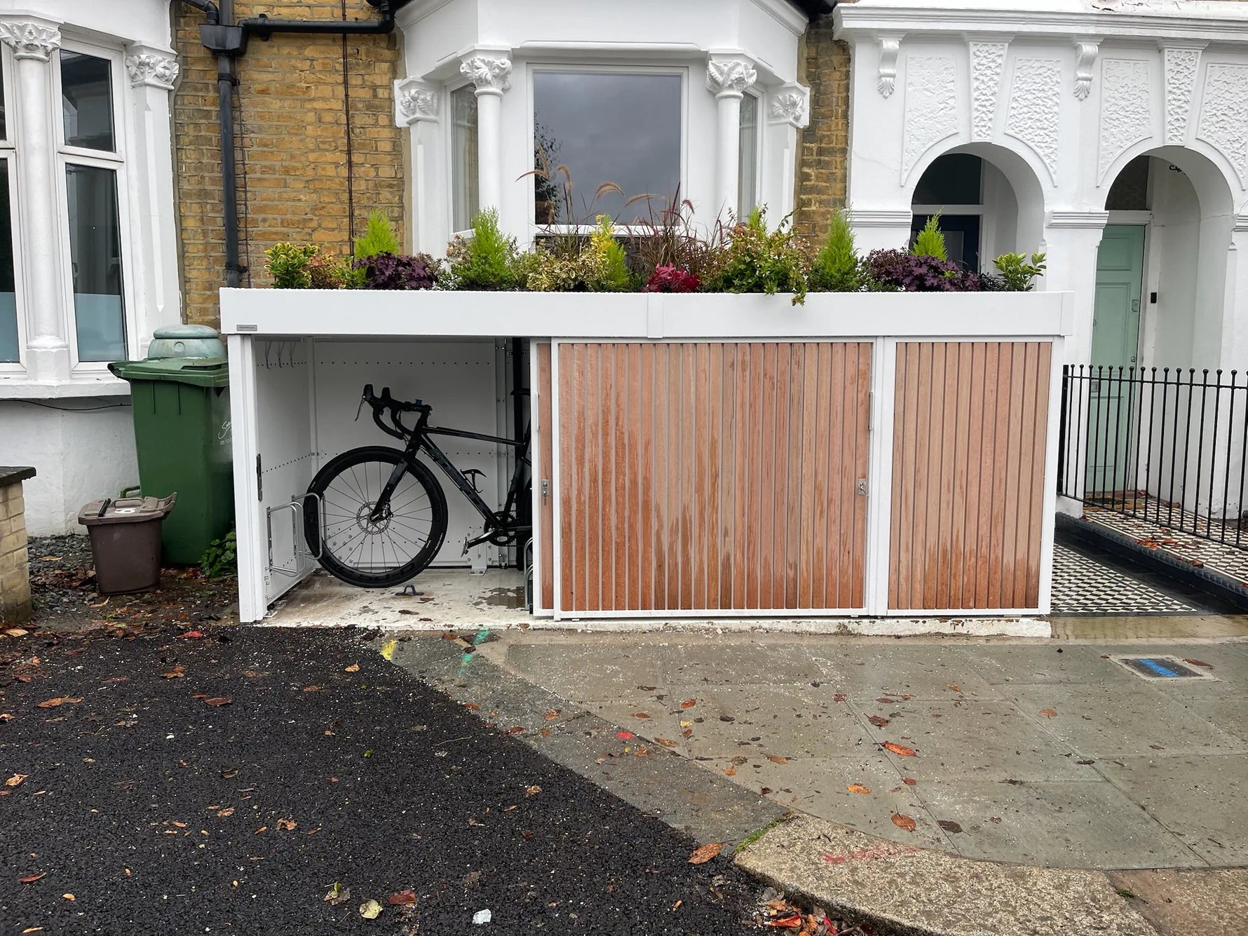 Bike store with left sliding door open, providing easy access to cycle storage in small London front garden.