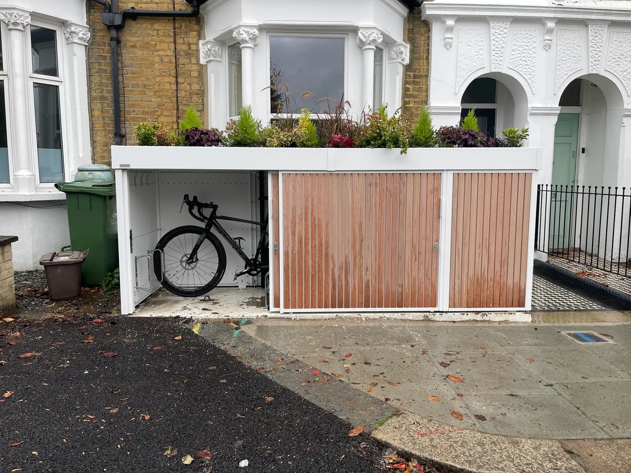 Bike store with left sliding door open, providing easy access to cycle storage in small London front garden.