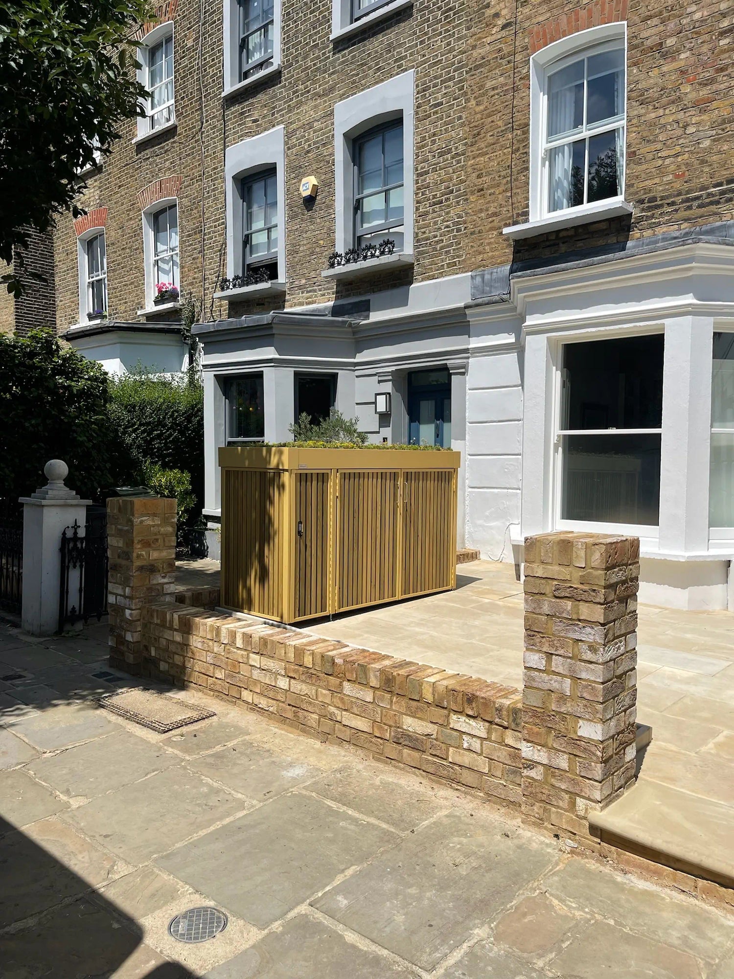  Full-angle view of closed bin and parcel box with timber cladding and green roof in a landscaped London front garden.