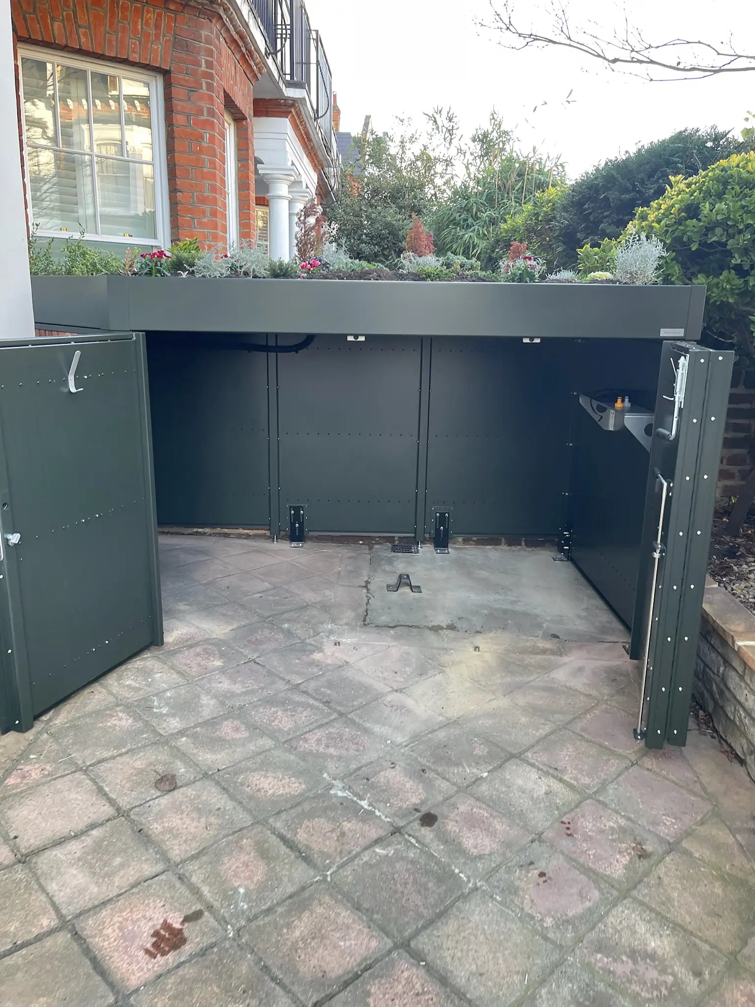 Fully open deep green bike store revealing full-depth storage in a London front garden conservation area