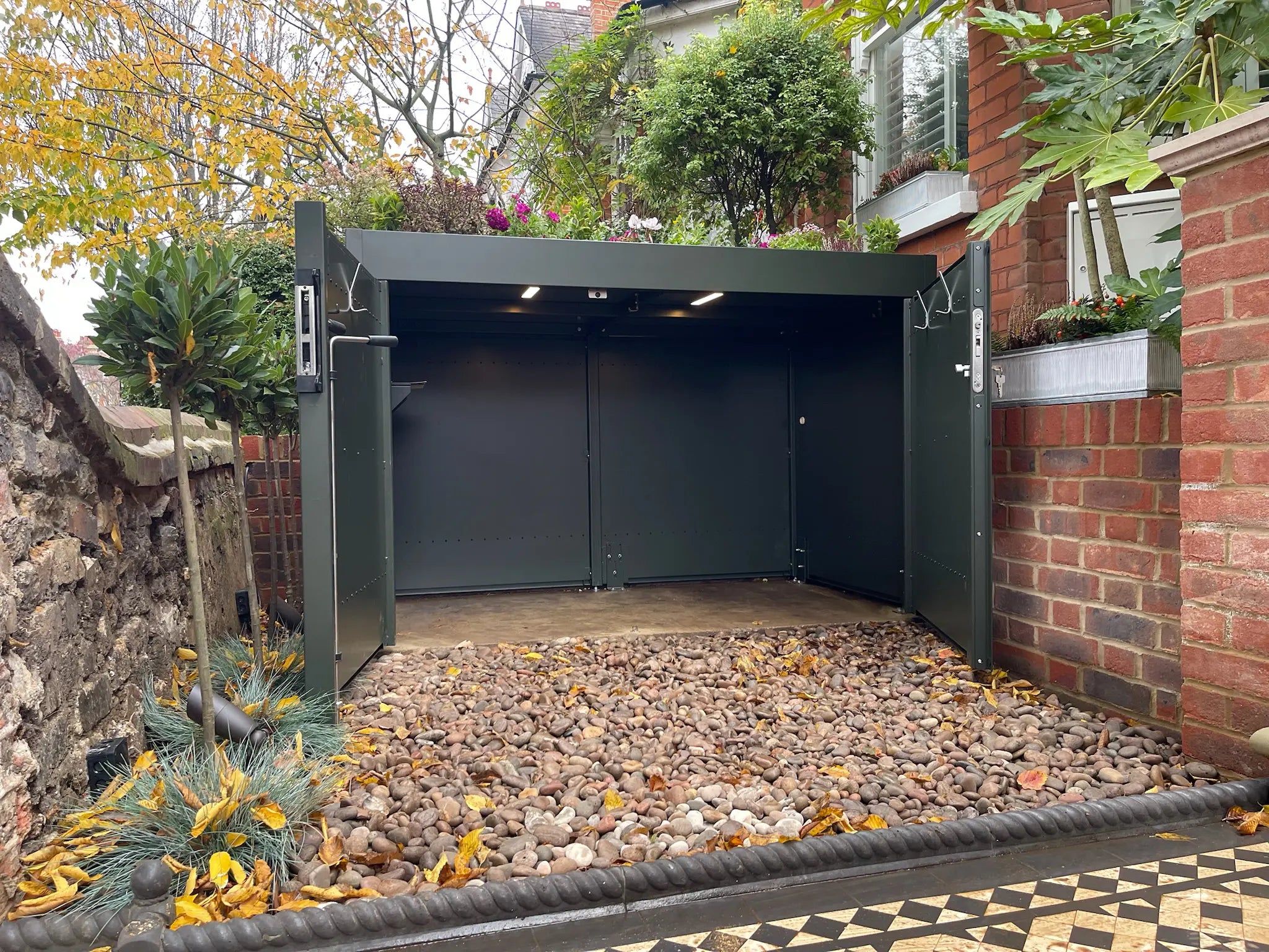 Interior view of deep green bike store with full-width hinged doors fully open for easy access to bikes and prams