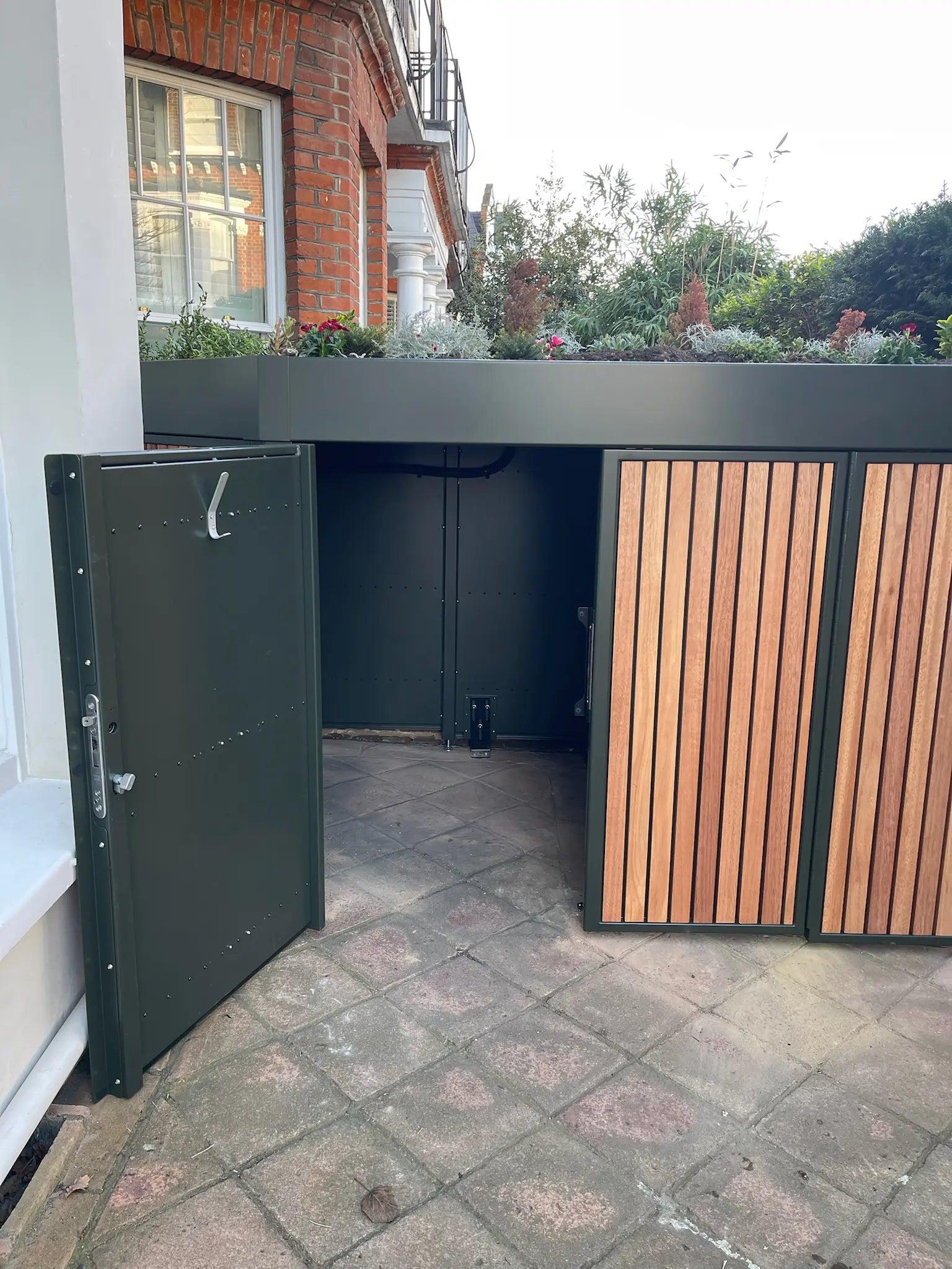 Left door open on deep green bike store, allowing easy daily access from the front garden