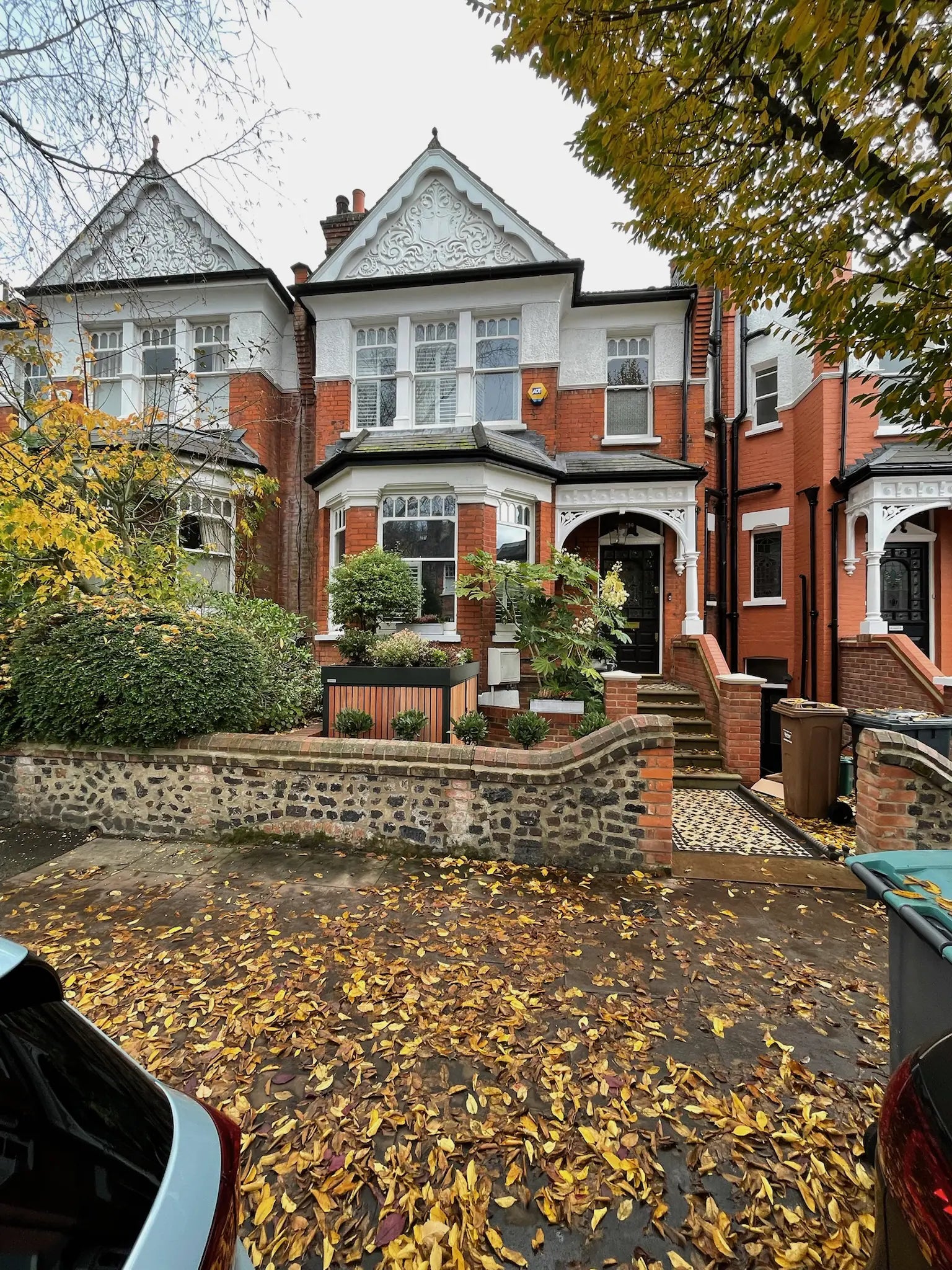 Frontal street view of deep green front garden bike store with timber cladding and planted roof on a London terrace