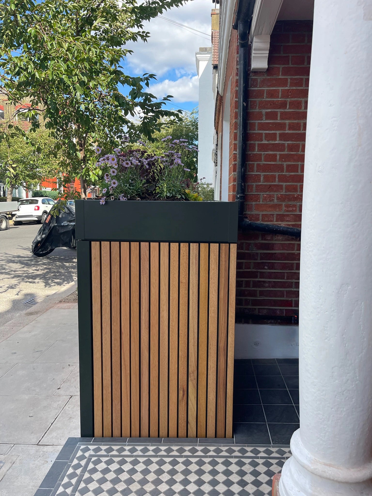 Close detail of the timber slatted door and handle on a front garden bike and bin store, with planting along the roofline.