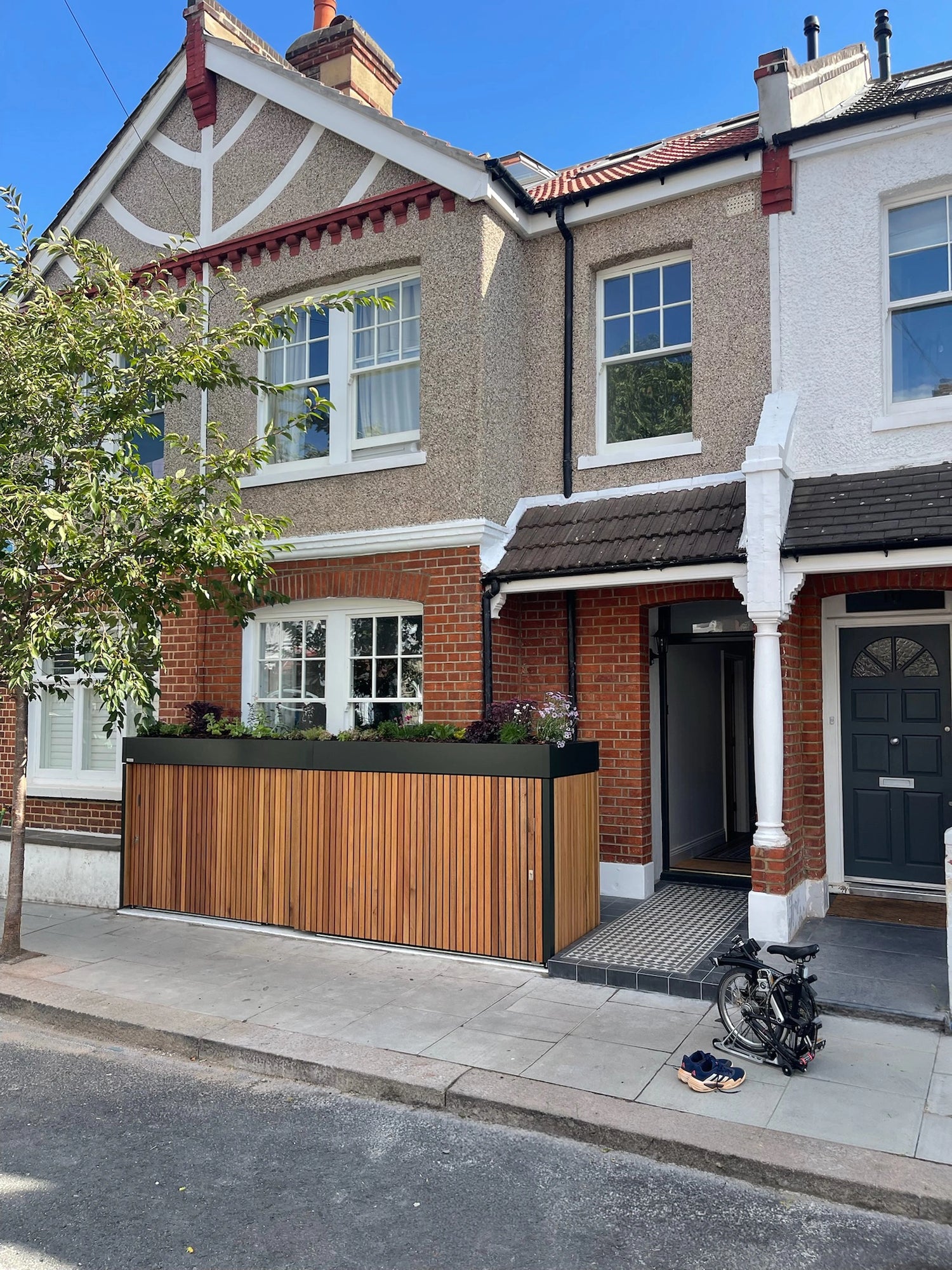Street view of a London terrace home with a timber-clad front garden bike and bin store built into the boundary line.