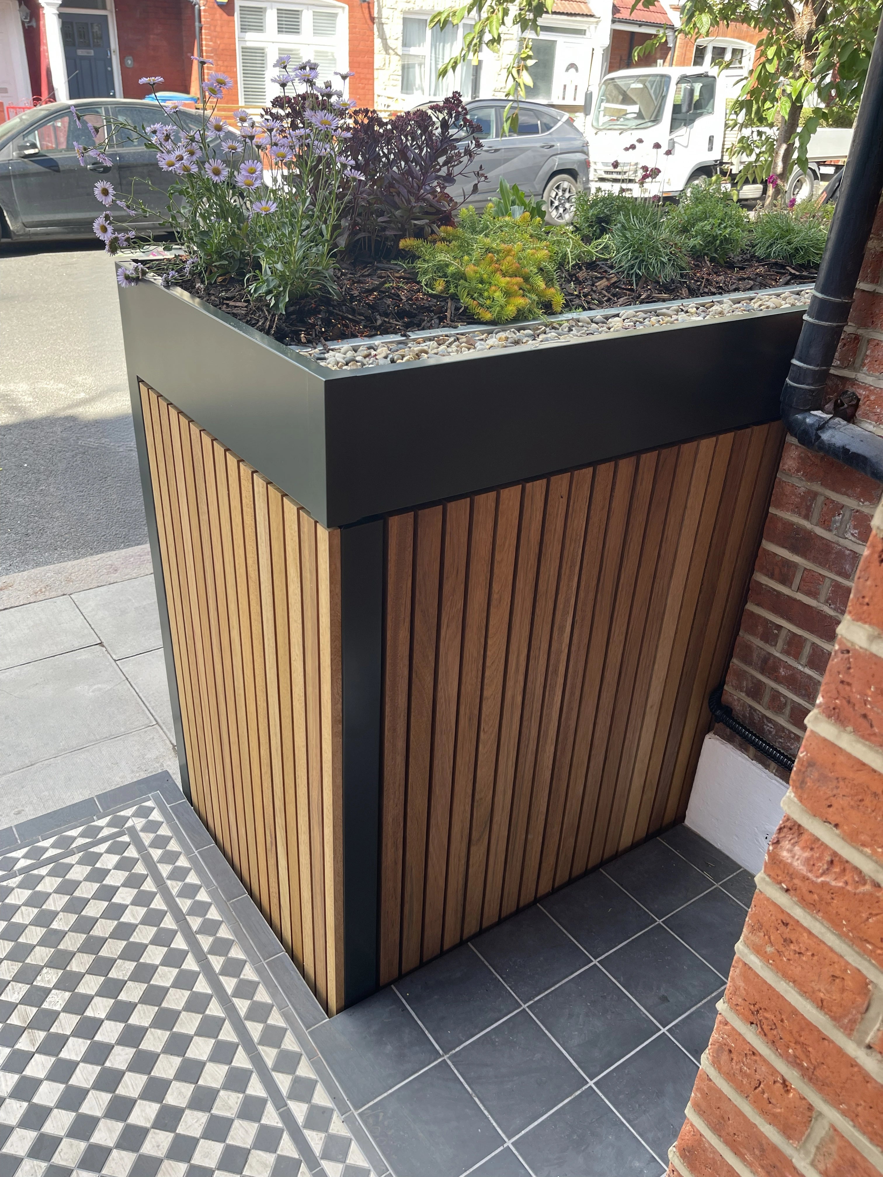 Corner detail of a front garden bike and bin store's planted roof, with pebble drainage and mixed planting above timber cladding.