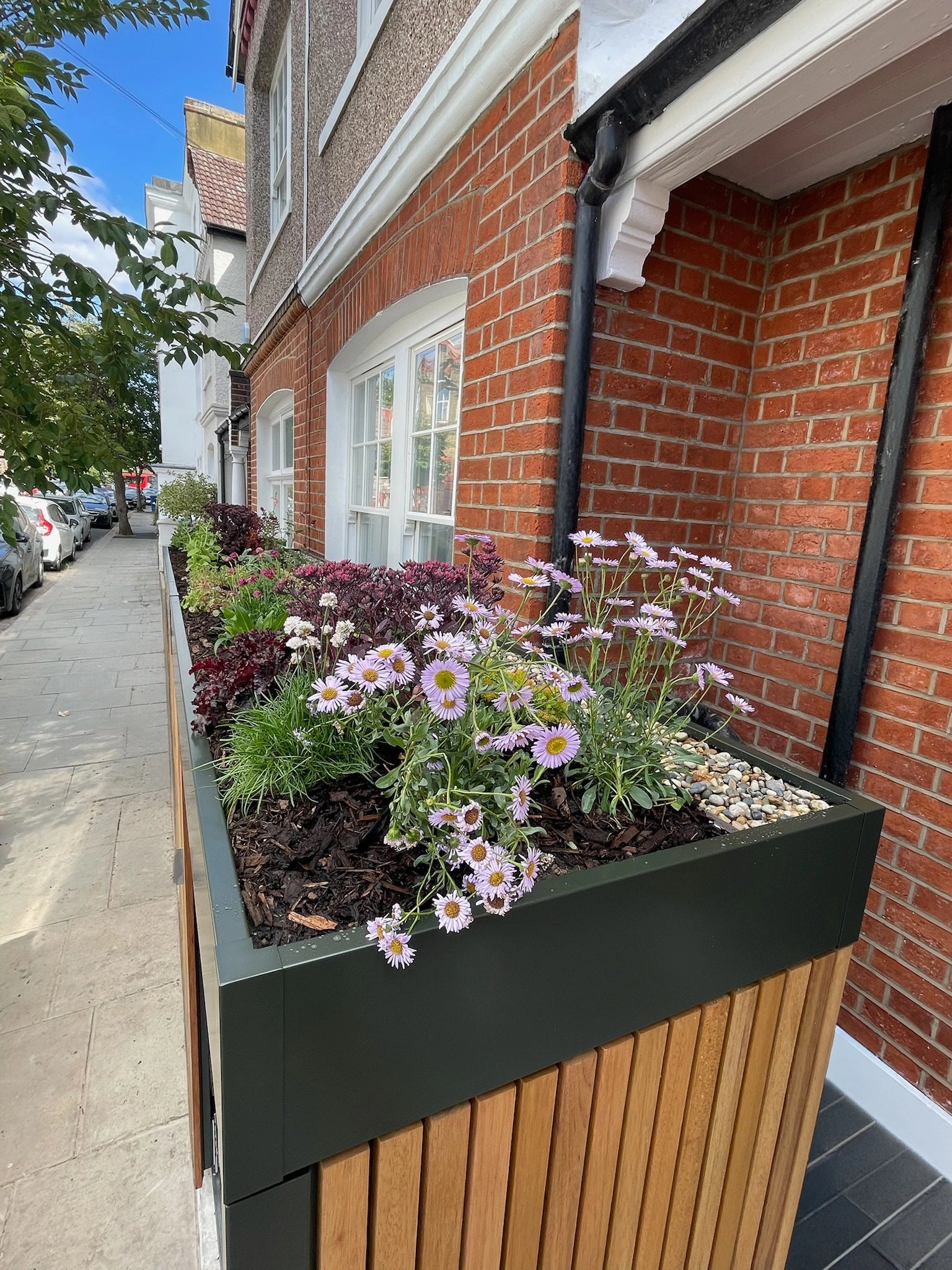 Planted roof detail of a front garden bike and bin store, with flowering plants and grasses against exposed London brickwork.