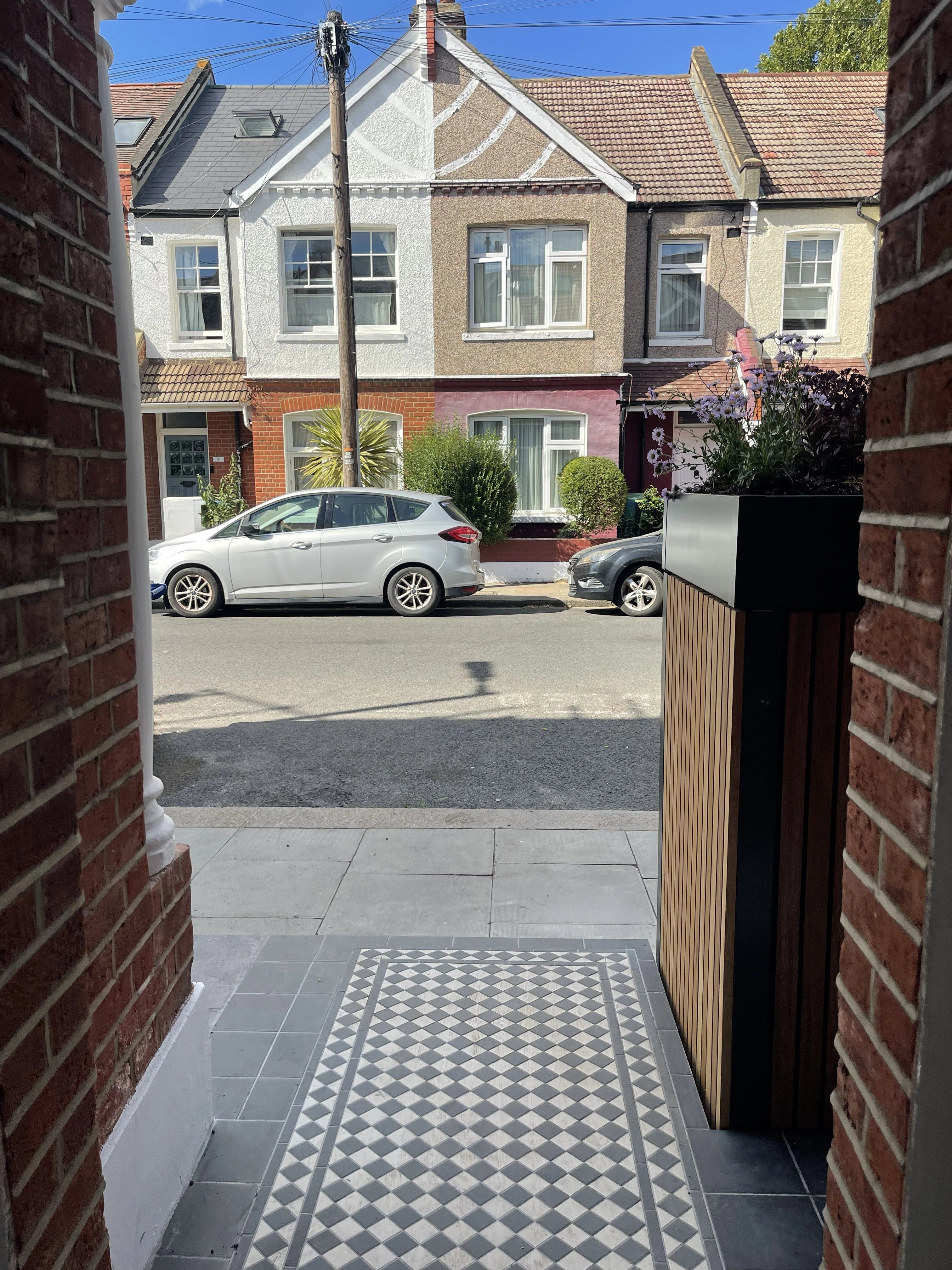 View from a London terrace's front porch across the mosaic-tiled path to the street, with the front garden bike and bin store alongside.