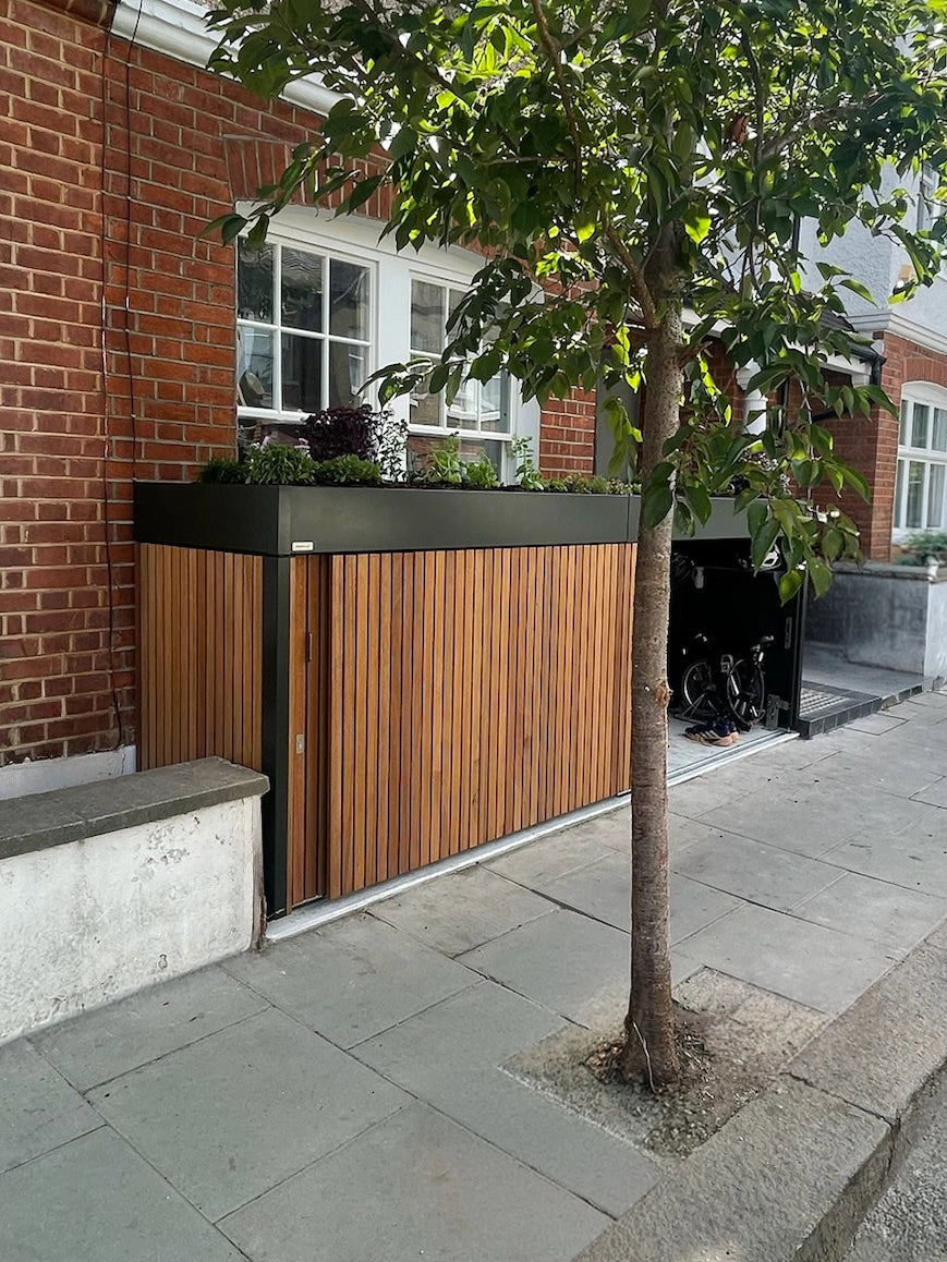 Distant street view of a London terrace with a front garden bike and bin store built into the boundary line.