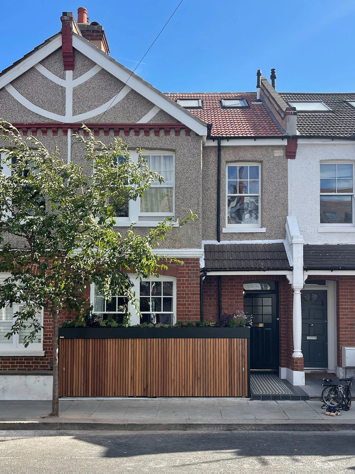 Front view of a London terrace home with an open front door beside a front garden bike and bin store.