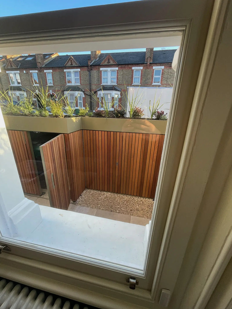 View from front room looking out onto redesigned front garden with integrated storage boundary and planting, doors open