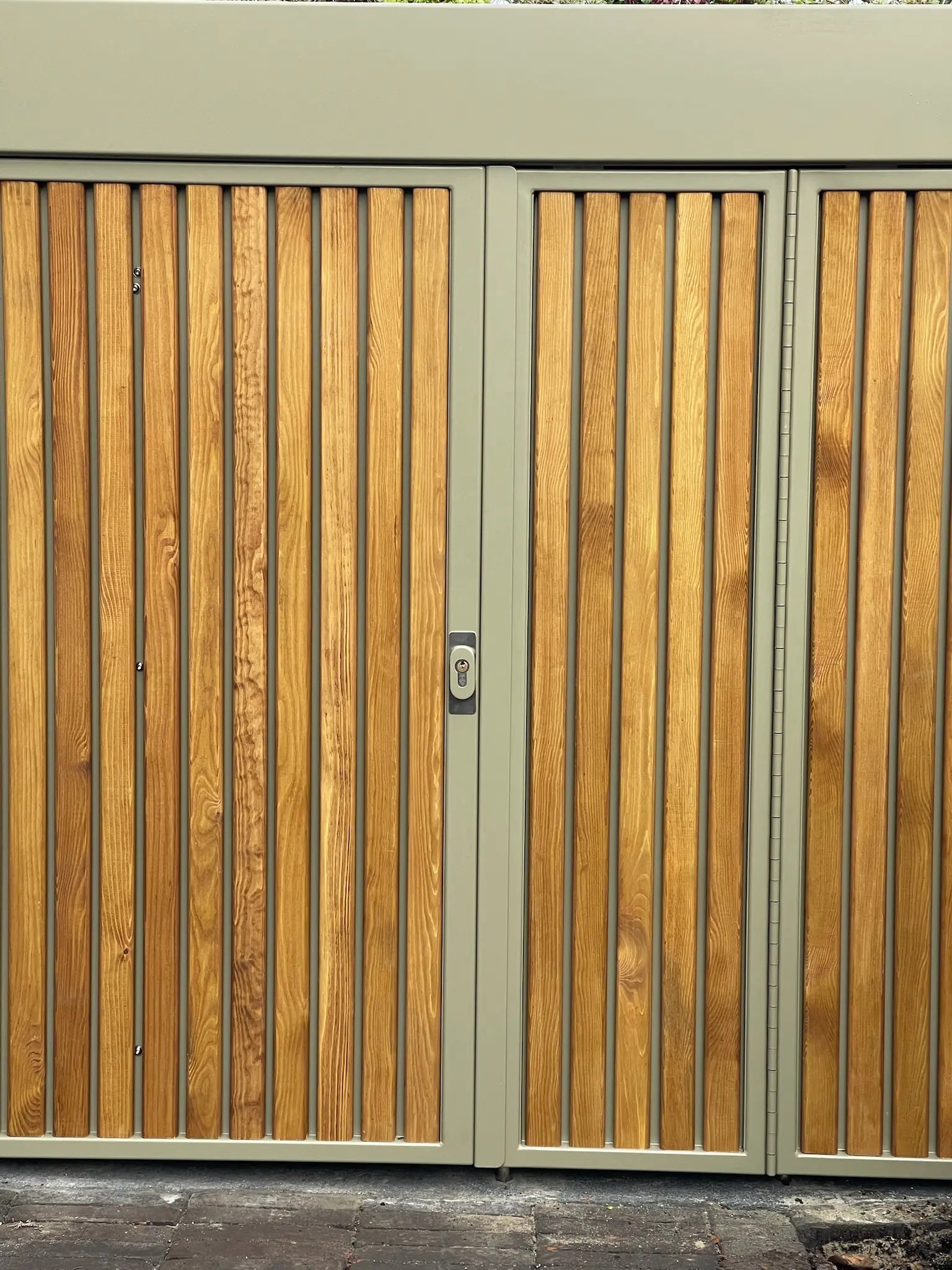 Walnut-stained timber cladding on olive-grey bike store in London front garden
