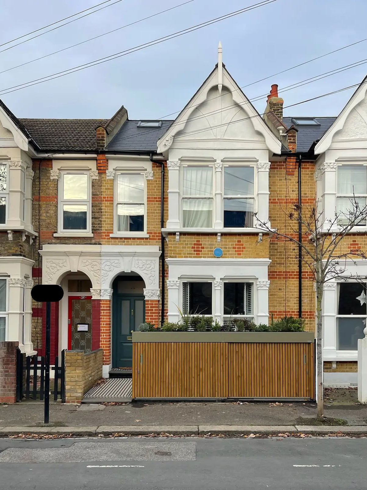 Closed olive grey bike and bin store with walnut-stained timber cladding, shown in context of a London terraced house frontage