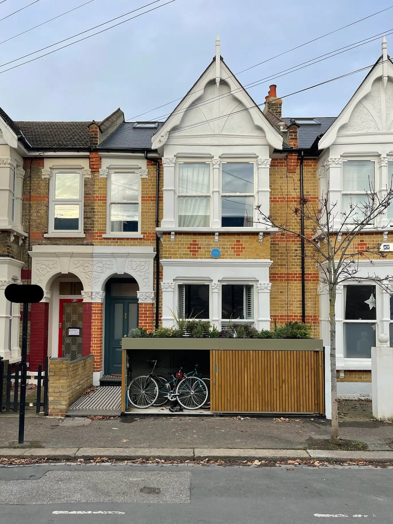Front view of olive grey bike store with walnut-stained timber cladding, doors open to reveal secure bike storage in a London front garden