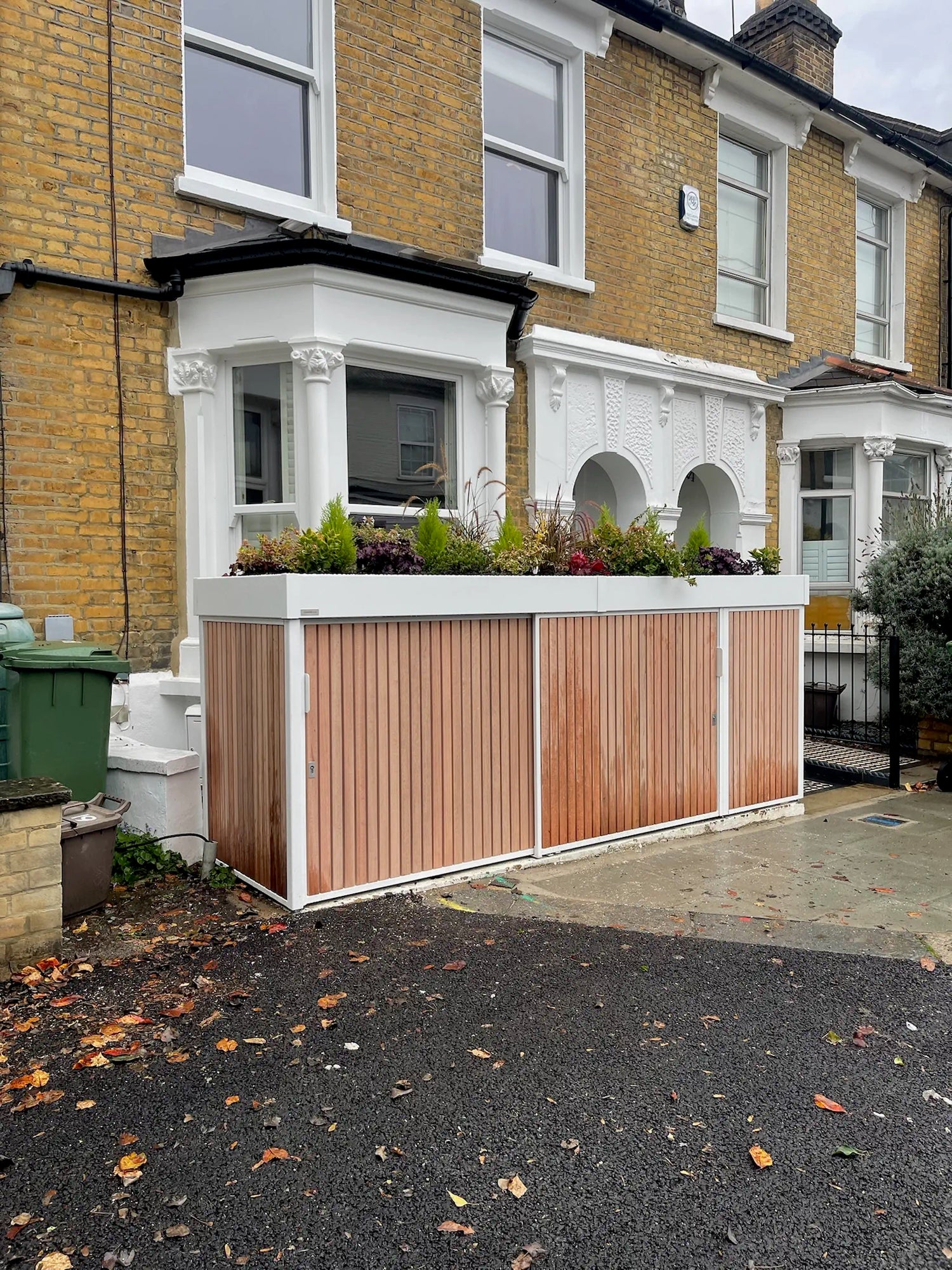 Closed front view of compact secure bike store with hardwood cladding and planted roof in London front garden.