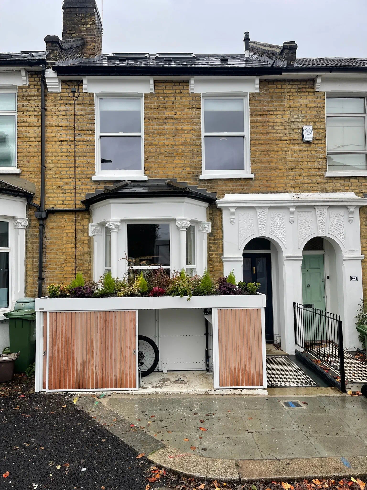 Secure cycle storage unit with right sliding door open, showing bike inside in compact front garden.