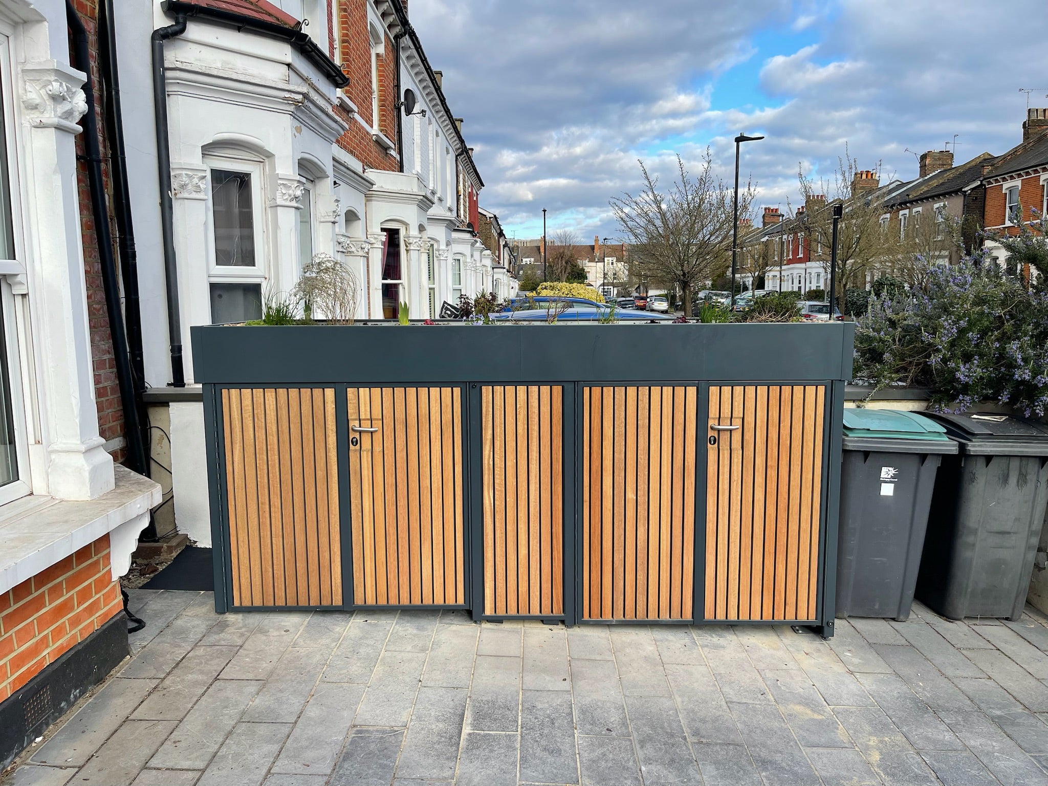 Single compartment double home bike storage unit seamlessly integrated into a sloped London driveway, preserving car access and enhancing front garden aesthetics, front view of full enclosure